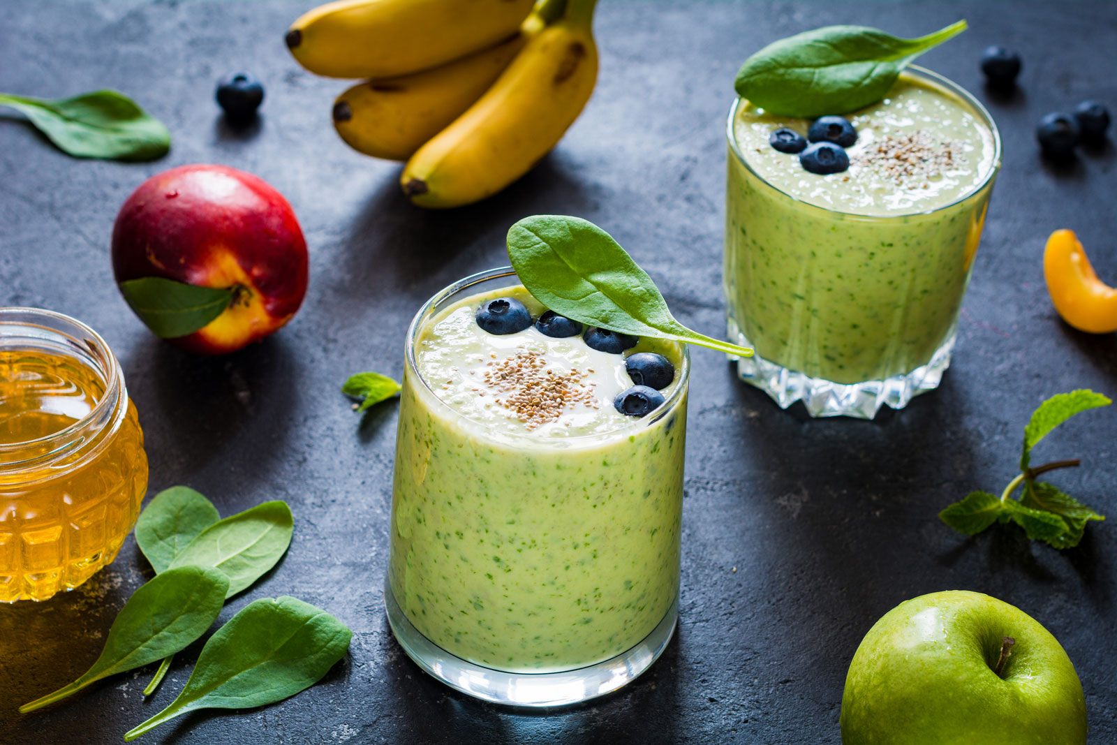 Detox green smoothies. Still life of green smoothie with fruits, honey and spinach leaves. Ultra healthy detox green smoothie with spinach, chia seeds, bananas, green apple, plain yogurt and honey on slate background